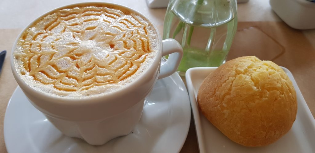 Xícara de café com pão de queijo em mesa de madeira
