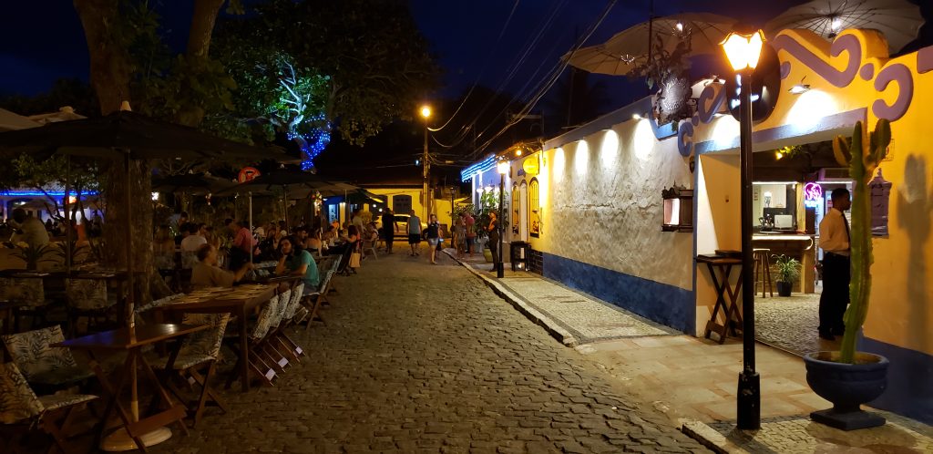 Rua iluminada com restaurantes e árvores ao entardecer